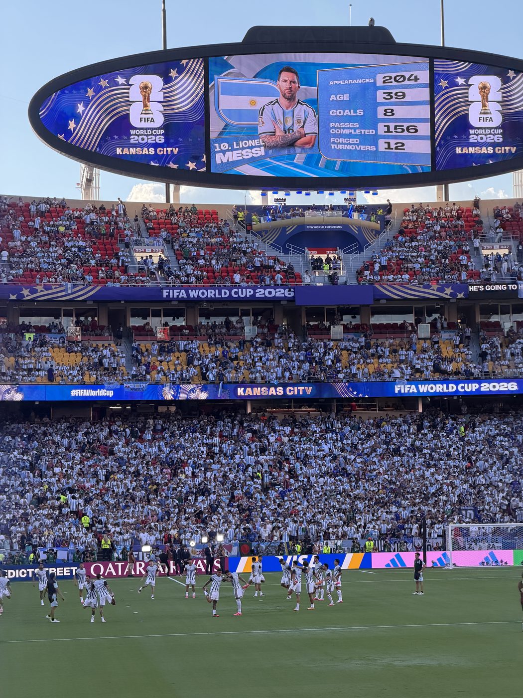 Arrowhead Stadium at the 2026 World Cup — Messi on the giant screen, Argentina warming up on the pitch, the stands full of blue and white
